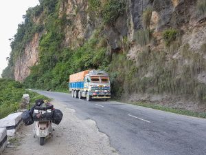 Lambretta parcheggiata lungo una strada di montagna in Nepal mentre passa un tipico camion nepalese colorato.