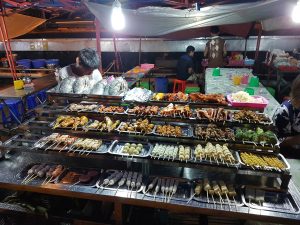 Bancarella di street food al mercato serale di Yangon con spiedini, pesce, verdure e specialità della cucina birmana.