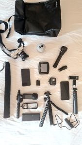 Fotocamera, action cam, navigatore TomTom, power bank, torce e accessori fotografici disposti sul letto.