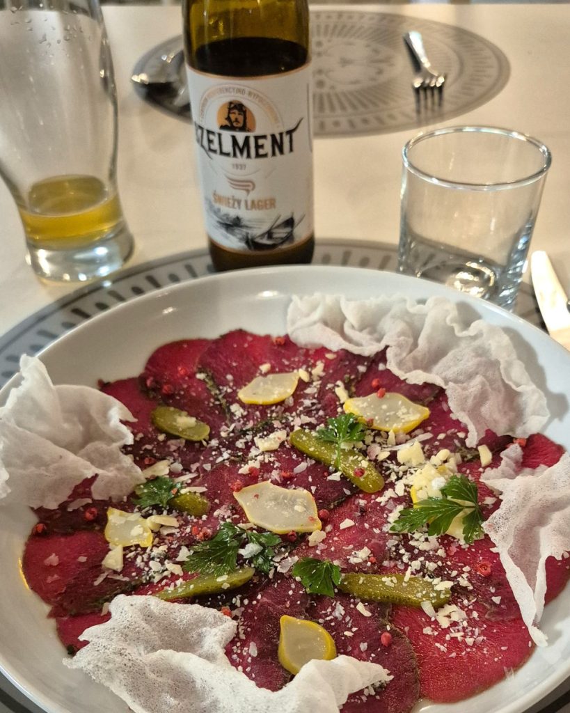 Carpaccio di cervo con cetriolini, limone, erbe aromatiche e guarnizioni croccanti, servito in un ristorante polacco.