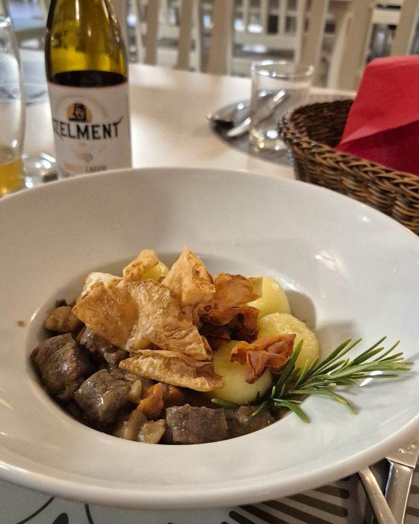 Gulasch di cinghiale servito con gnocchi di patate ripieni, guarnizione croccante e un rametto di rosmarino, in un piatto bianco.