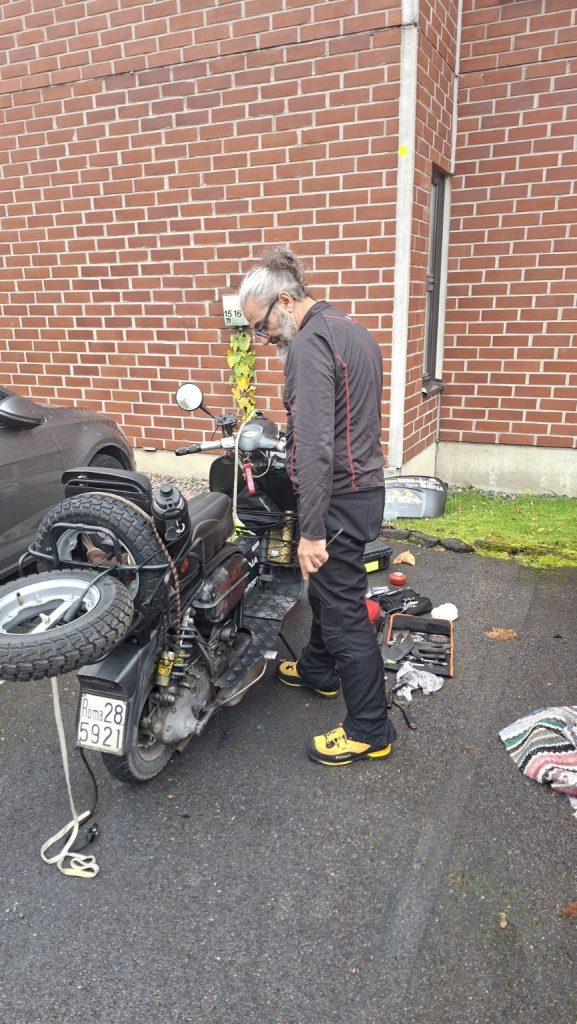 Filippo controlla la Lambretta Xena durante una riparazione a Helsinki, in Finlandia, con gli attrezzi sistemati sull'asfalto.