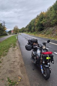 Lambretta grigia carica di bagagli parcheggiata lungo una strada austriaca, circondata da alberi con i primi colori autunnali.