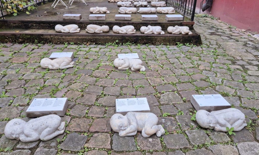 Installazione For Life a Riga, con piccole sculture di bambini non nati disposte sul selciato accanto a targhe informative.