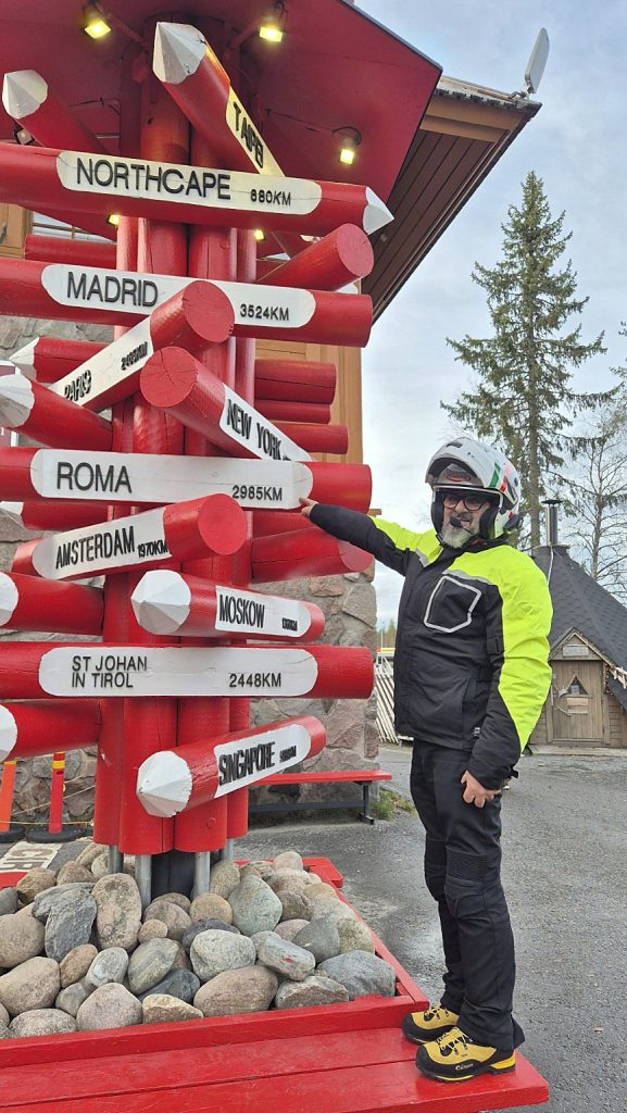 Filippo indica il cartello per Roma al Villaggio di Babbo Natale di Rovaniemi, in Lapponia, vicino al Circolo Polare Artico.