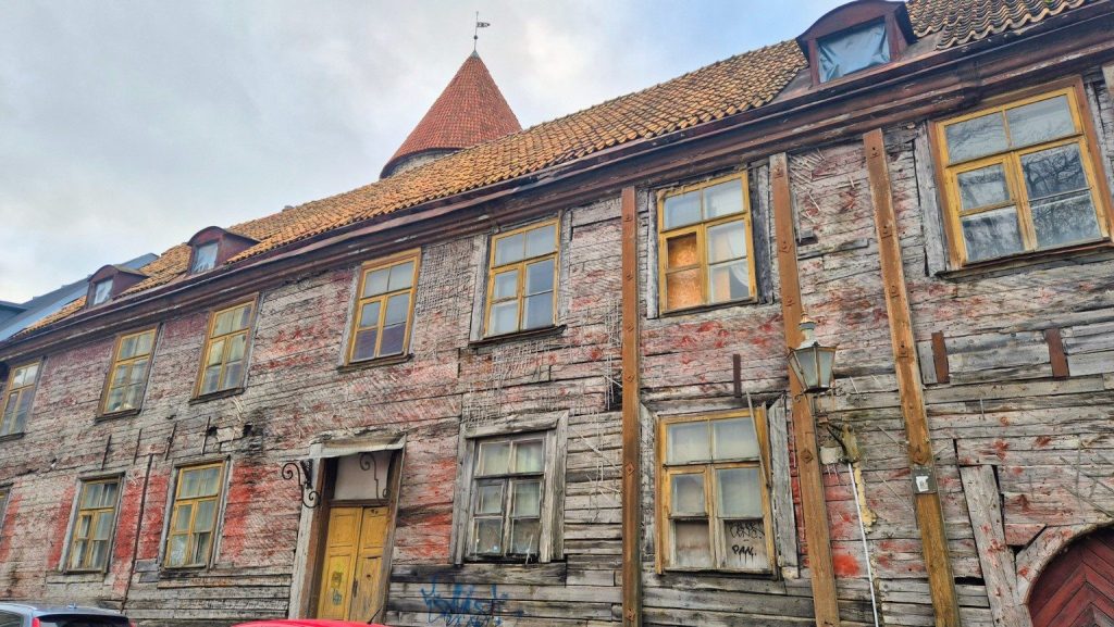 Antico edificio in legno a Tallinn, Estonia, con facciata consumata dal tempo, finestre gialle e tetto in tegole.