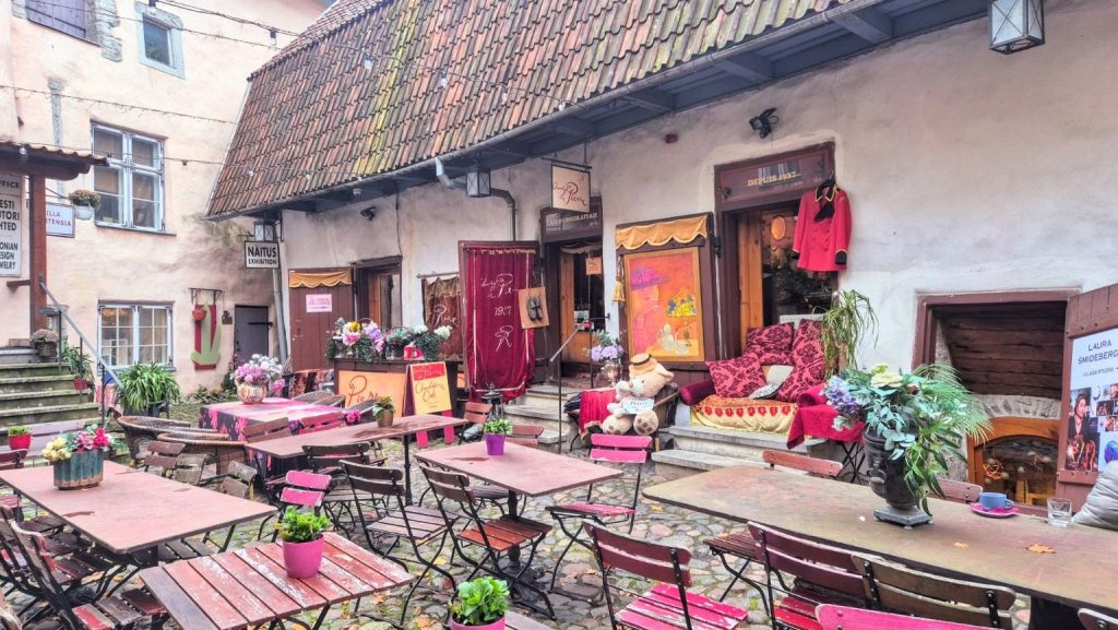 Cortile dei Maestri a Tallinn, con i tavolini del Café Pierre, fiori colorati e botteghe artigiane nel centro storico.
