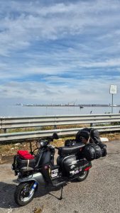 Lambretta carica di bagagli in sosta lungo la Romea, nei pressi di Chioggia, con la Laguna Veneta sullo sfondo.